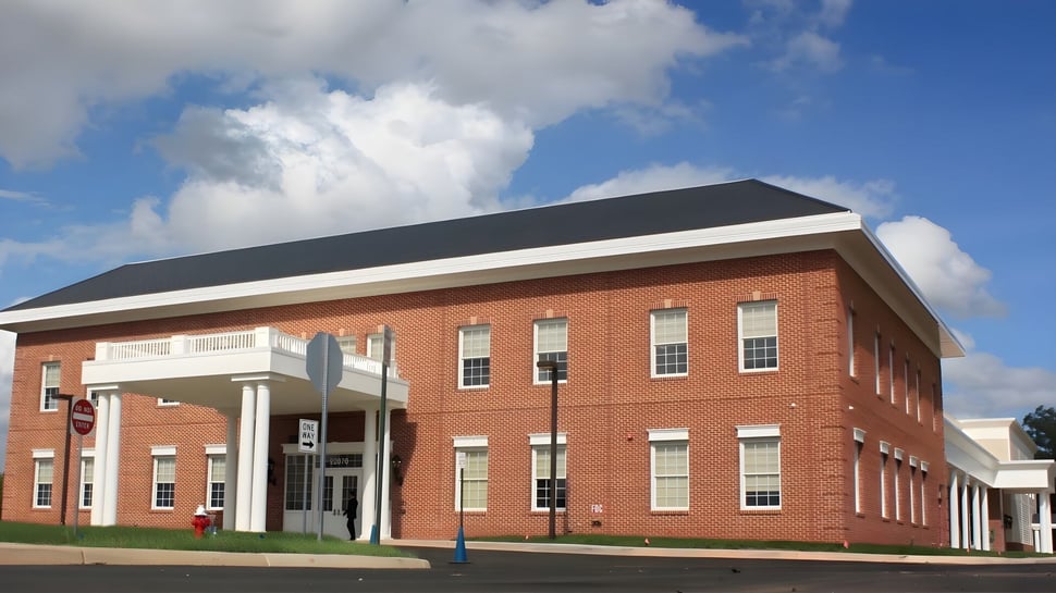 El edificio de ladrillo de la Fairfax Christian School con una entrada distintiva y techo inclinado frente a un cielo azul.