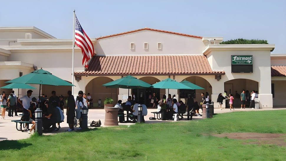Estudiantes de la Fairmont Prep Academy están frente al edificio de estilo español con sombrillas verdes.