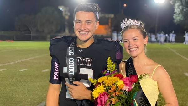 Un hombre en una camiseta de fútbol está junto a una mujer con corona y flores en el campo de fútbol de la Faith Christian Academy en Florida.