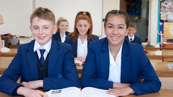 Un grupo de estudiantes sonrientes en uniforme escolar está sentado en el aula de la Farlington School en sus escritorios.