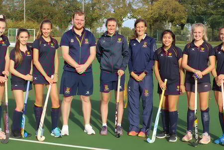 Un grupo de jóvenes jugadoras y jugadores de hockey está reunido en el campo deportivo de la Felsted School.