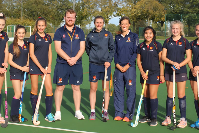 Un grupo de jóvenes jugadoras y jugadores de hockey está reunido en el campo deportivo de la Felsted School.