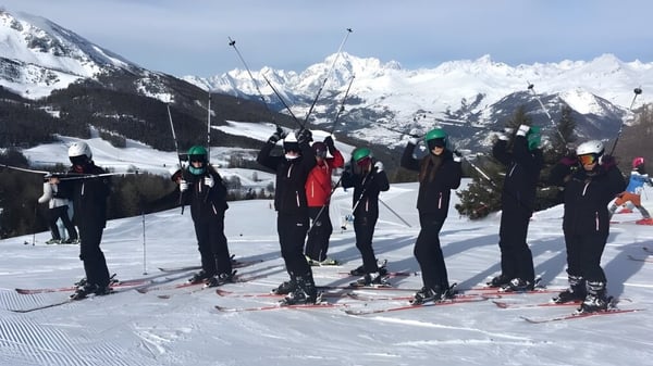 Un grupo de estudiantes de la Ferndown Upper School está en una pendiente cubierta de nieve con montañas de fondo.