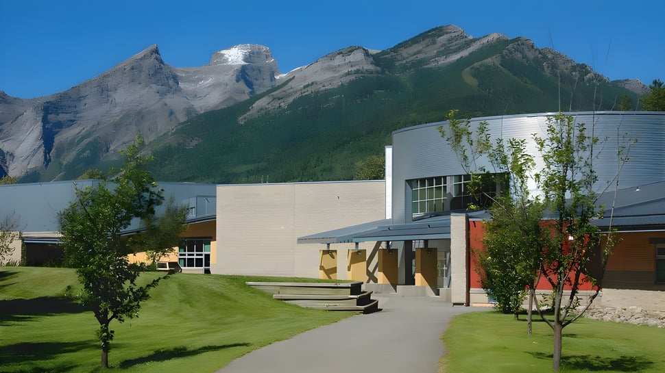 El moderno edificio de la Fernie Secondary School se encuentra frente a una superficie de césped con montañas al fondo bajo un cielo despejado.