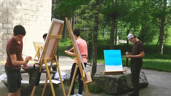 Estudiantes de la Fernie Secondary School participan en una actividad de pintura al aire libre en el bosque verde.