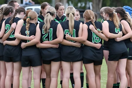 Un grupo de jóvenes deportistas está en un campo deportivo de la Ferny Grove State High School frente a árboles y edificios.