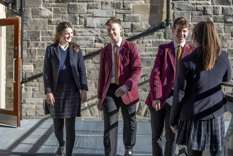 Cuatro personas en ropa formal están de pie frente a un edificio de piedra en el campus del Fettes College.