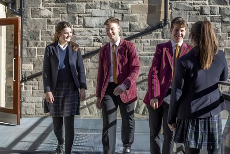 Cuatro personas visten ropa formal y están de pie frente a un edificio de piedra en el campus del Fettes College.