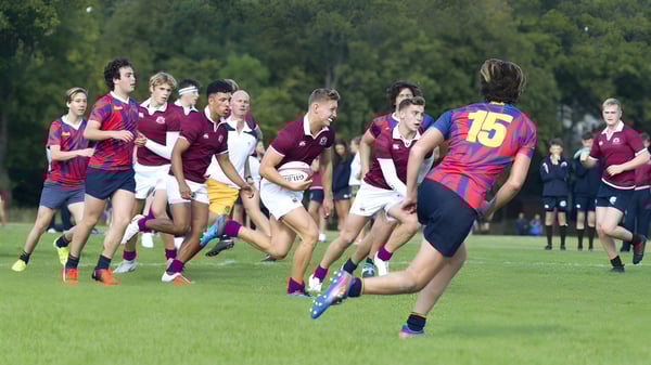 Estudiantes del Fettes College juegan un partido de rugby en un campo de hierba con árboles al fondo.
