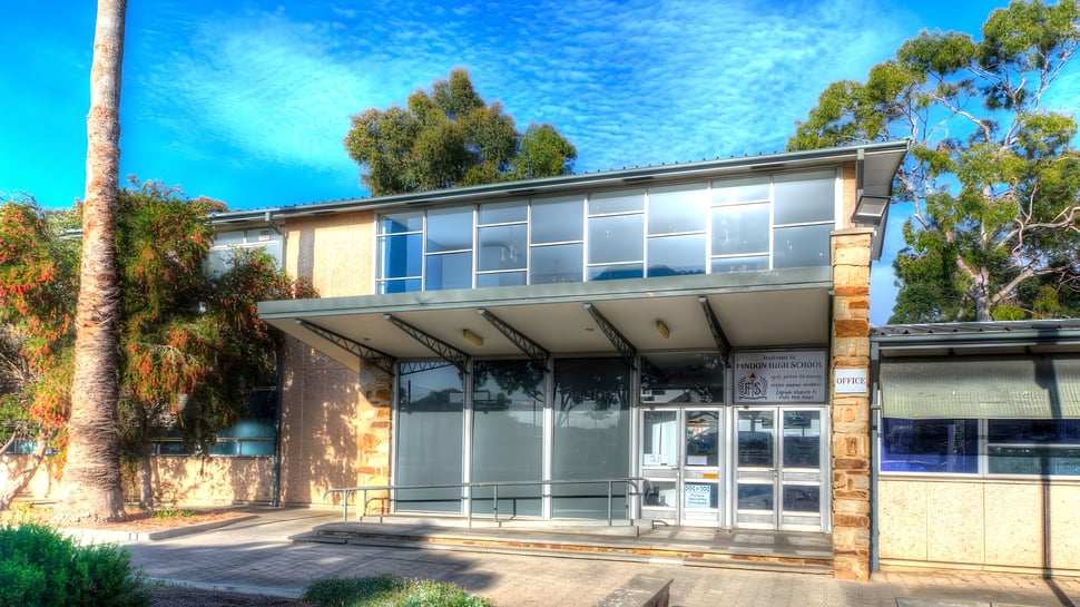 El moderno edificio de vidrio de Findon High School está rodeado de vegetación verde y se encuentra bajo un cielo azul claro.