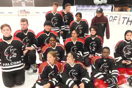 Un grupo de jóvenes jugadores de hockey posan en uniformes negros y rojos sobre el hielo de Findon High School.