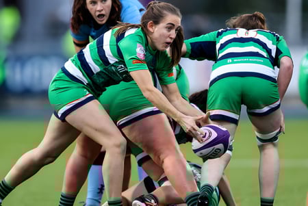 Un grupo de jugadoras de rugby en uniformes verdes y blancos en un scrum en el campo del Fingal Community College.
