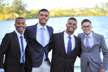 Cuatro hombres en ropa formal están juntos frente a un cuerpo de agua en el terreno de la Florida Preparatory Academy.