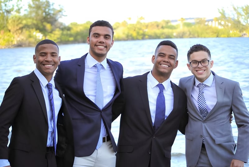 Cuatro hombres en ropa formal están juntos frente a un cuerpo de agua en el terreno de la Florida Preparatory Academy.