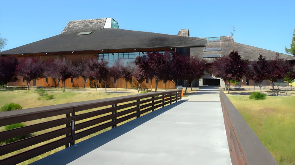 El moderno edificio con un techo distintivo en Foothill College está rodeado por una cerca de madera y un camino de piedra.