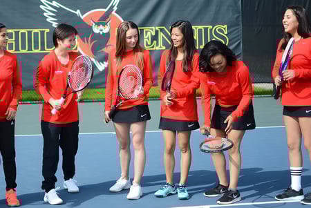 Un grupo de estudiantes en uniformes deportivos rojos está reunido en la cancha de tenis de Foothill College frente a un gran logo de ala.