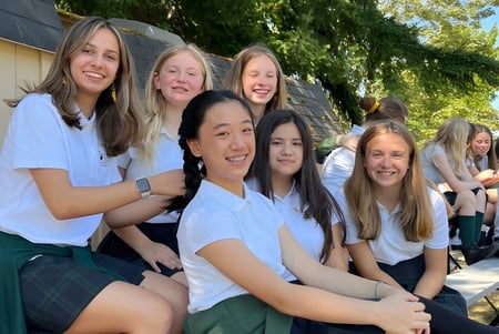 Un grupo de estudiantes sonrientes está afuera en el terreno de la Forest Ridge School of the Sacred Heart frente a una vegetación verde.