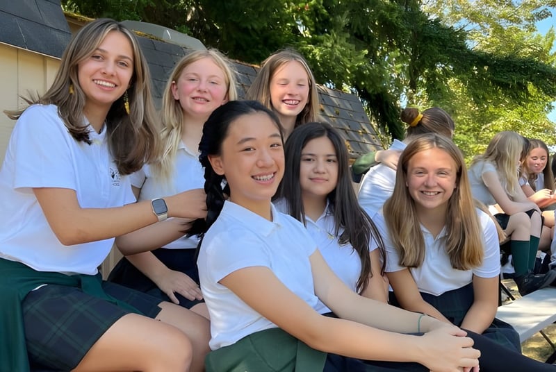 Un grupo de estudiantes sonrientes está afuera en el terreno de la Forest Ridge School of the Sacred Heart frente a una vegetación verde.