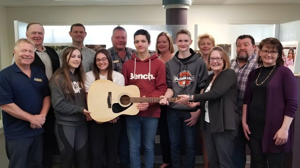 Un grupo de estudiantes de la Forestburg School toca música juntos en un interior con un guitarrista en el centro.