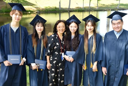 Un grupo de graduados de la Forsyth Country Day School está de pie con ropa académica frente a un paisaje con agua.