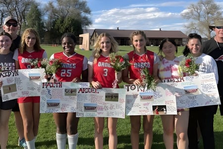 Un grupo de jóvenes deportistas está en el campo deportivo de la Fountain Valley School of Colorado con carteles de apoyo.