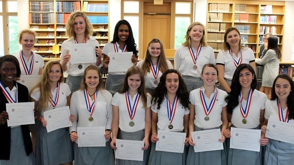 Un grupo de alumnos de la Foxcroft School está con medallas en una biblioteca frente a estanterías de libros.
