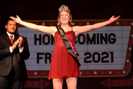 Una joven con vestido rojo y corona está con los brazos levantados en el evento de Homecoming en la Fox Valley Lutheran High School.
