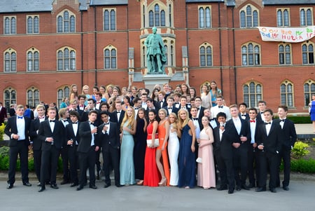 Un gran grupo de estudiantes está vestido de manera formal frente a un edificio histórico en el campus de Framlingham College.