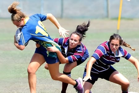 Tres alumnas del Fraser Coast Anglican College participan en una competencia deportiva en un campo de hierba.
