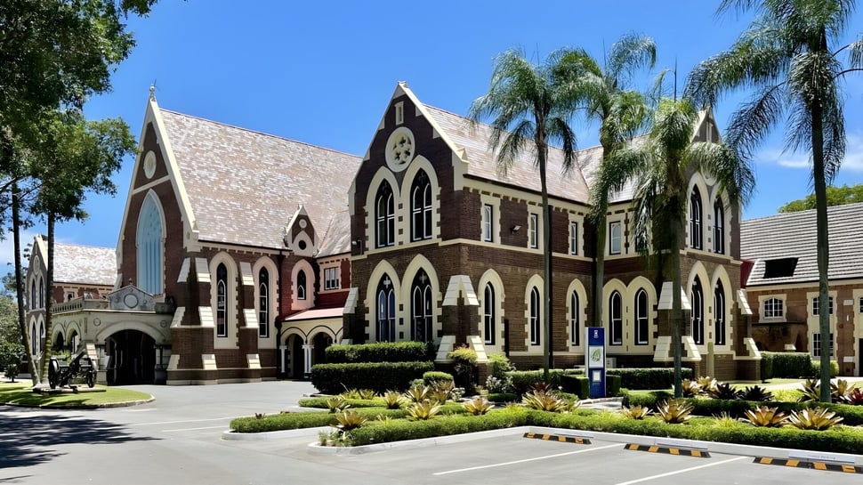 El representativo edificio de ladrillo con torre y ventanas de arco en el terreno del Fraser Coast Anglican College está rodeado de palmeras.