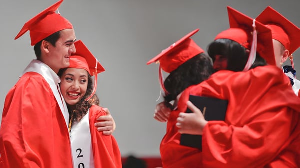 Estudiantes de la Freedom Preparatory Academy celebran juntos en togas y birretes rojos su éxito.
