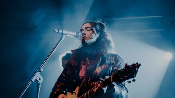 Una estudiante del Fremantle College toca la guitarra y canta en el escenario bajo luz azul.