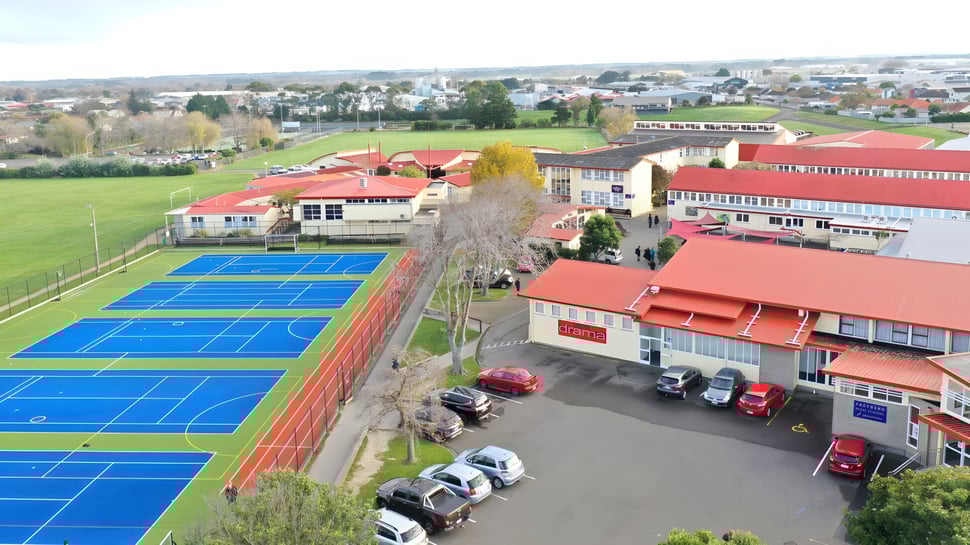 La cancha de tenis en el terreno de la Freyberg High School muestra coloridos campos de juego al aire libre con edificios de fondo.