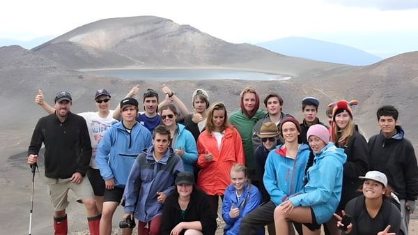 Un grupo de estudiantes de la Freyberg High School posan frente a un pintoresco paisaje montañoso con un lago.