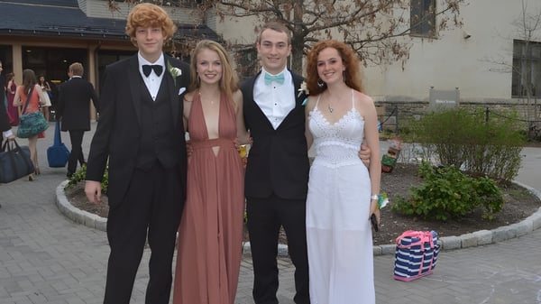 Cuatro estudiantes de la Friends School of Baltimore están juntos vestidos formalmente en el exterior frente a un camino pavimentado.
