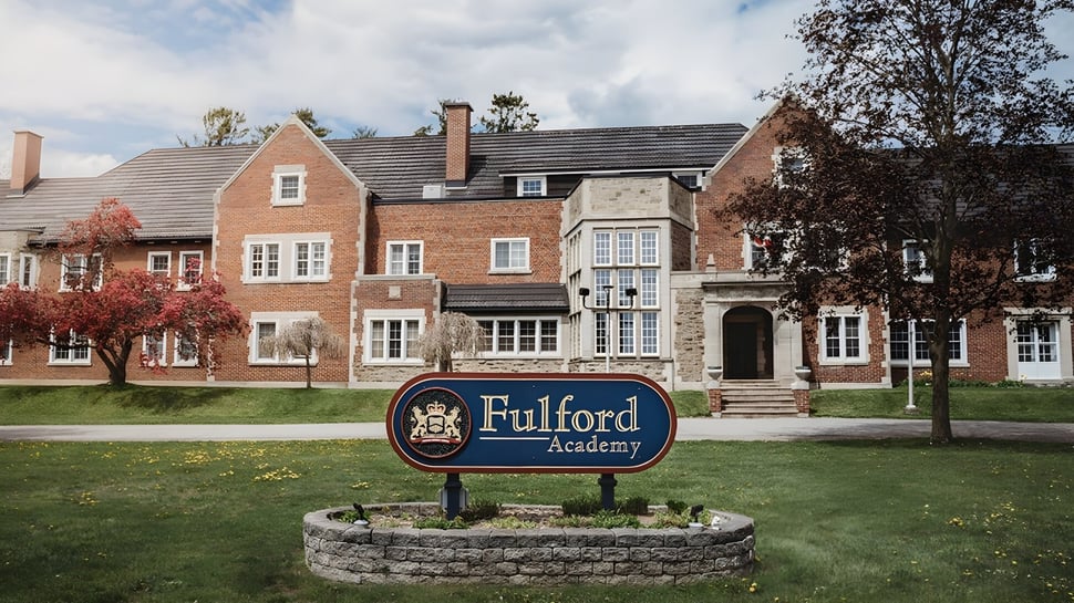 El edificio de ladrillo y piedra de la Fulford Academy se encuentra en un área verde con árboles y otros edificios similares en los alrededores.