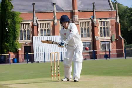 Un estudiante de la Fulneck School está en equipo de cricket en un campo de césped frente a un edificio de ladrillo.