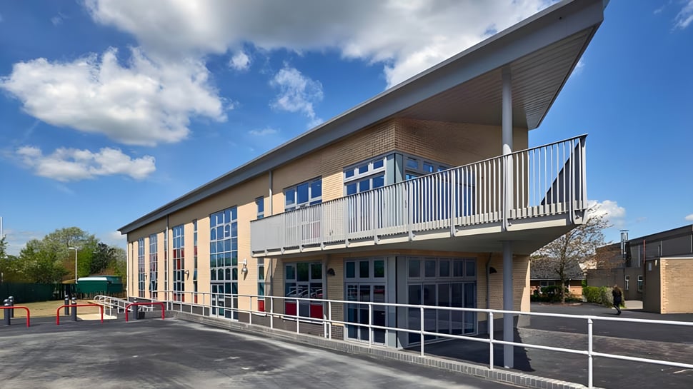 El moderno edificio escolar de la Fulston Manor School con grandes ventanas y balcón bajo un cielo azul.