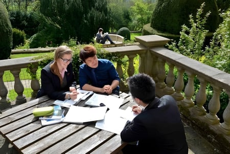 Un grupo de estudiantes de la Fyling Hall School se reúne en una mesa en la terraza de madera en un jardín.