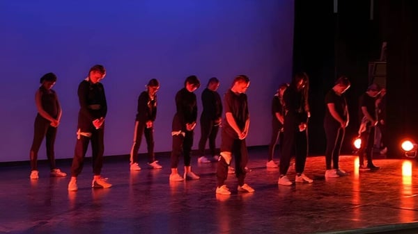 Estudiantes de la G.W. Graham Secondary School están en una sala de teatro con iluminación roja y azul.