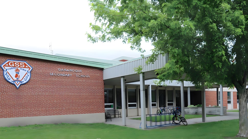 El edificio de ladrillo de la Gananoque Secondary School está rodeado de árboles verdes y un prado.
