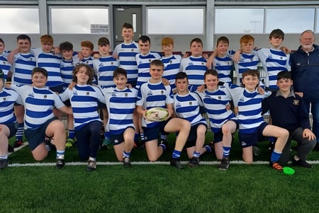 Un grupo de jóvenes jugadoras de rugby del Garbally College está reunido en un campo de juego frente a una instalación deportiva.