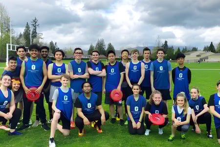 Un grupo de estudiantes en uniforme azul está en un campo de hierba frente a árboles en el terreno de la Garibaldi Secondary School.