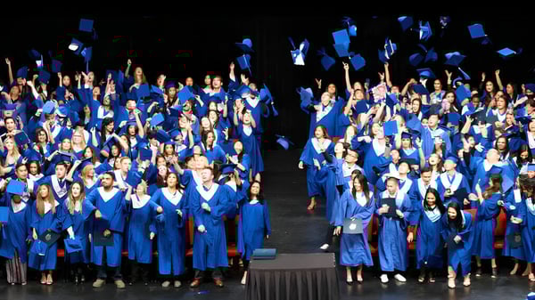 Un grupo de estudiantes de la Garibaldi Secondary School lleva túnicas de graduación azules en una ceremonia de graduación en un escenario.