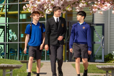 Tres alumnos en uniformes escolares están frente a un edificio en el campus del Garin College con flores de cerezo de fondo.
