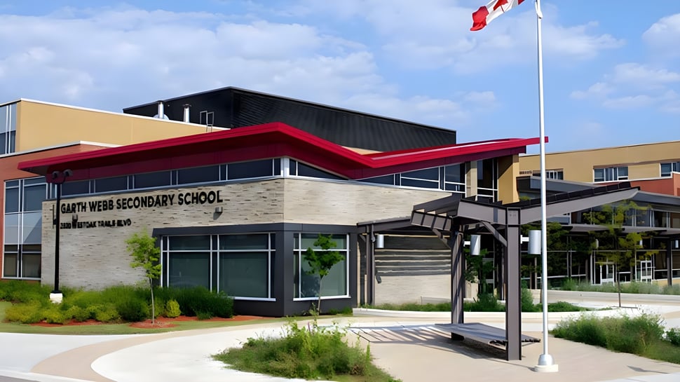 El moderno edificio de varios pisos de la Garth Webb Secondary School con un toldo rojo y la bandera canadiense delante.