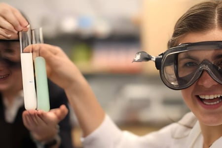 Una mujer lleva gafas de protección y sostiene un recipiente de vidrio en el laboratorio de la Gaston Day School.