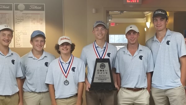 Un grupo de estudiantes de la Gaston Day School está de pie con un trofeo en el pasillo de la escuela frente a pizarras blancas.