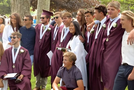 Un grupo de graduadas y graduados de la George Stevens Academy está en túnicas burdeos en el bosque.