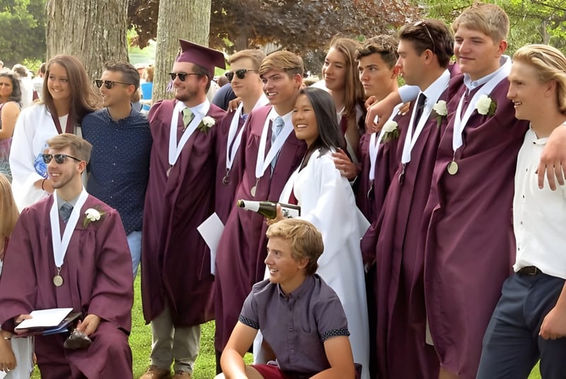 Un grupo de graduadas y graduados de la George Stevens Academy está en túnicas burdeos en el bosque.